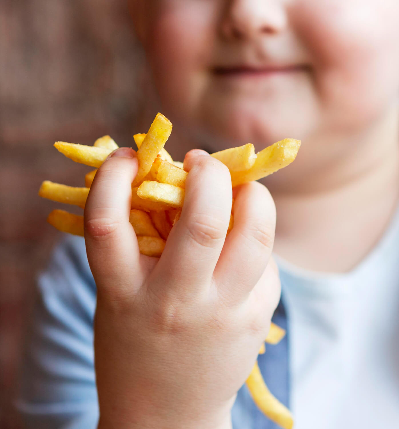An overweight boy with a handful of french fries