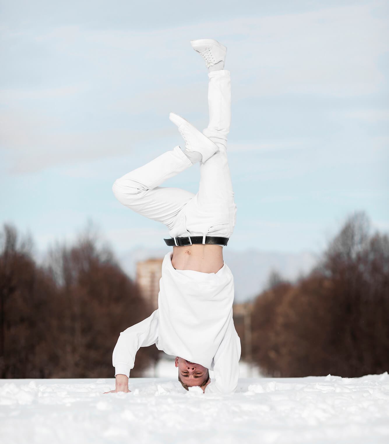 A man dressed all in white doing a headstand in the snow